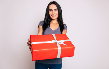 To you. Close up photo of a red box with a blue ribbon, held by a young beautiful girl with long dark hair and broad smile.