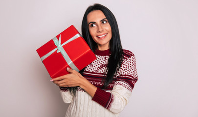 Wonder what inside? Cute girl in knitted reindeer sweater is holding a red present box near her...