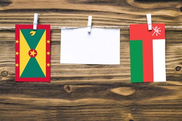 Hanging flags of Grenada and Oman attached to rope with clothes pins with copy space on white note paper on wooden background.Diplomatic relations between countries.