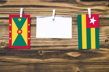 Hanging flags of Grenada and Togo attached to rope with clothes pins with copy space on white note paper on wooden background.Diplomatic relations between countries.