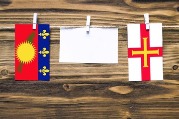 Hanging flags of Guadeloupe and Guernsey attached to rope with clothes pins with copy space on...