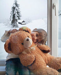 a girl sits on a windowsill with a toy, outside the window is winter.