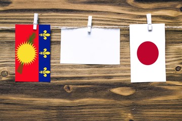 Hanging flags of Guadeloupe and Japan attached to rope with clothes pins with copy space on white...