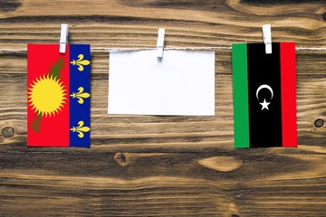 Hanging flags of Guadeloupe and Libya attached to rope with clothes pins with copy space on white note paper on wooden background.Diplomatic relations between countries.
