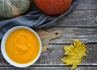 pumpkin soup in a deep plate and a yellow maple leaf on a gray wooden background with space for text.  flat lay