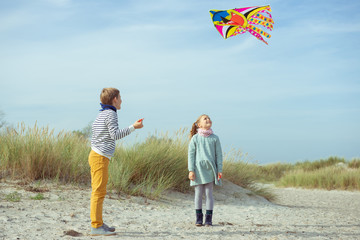 Happy siblings children running and having fun with kite on beach