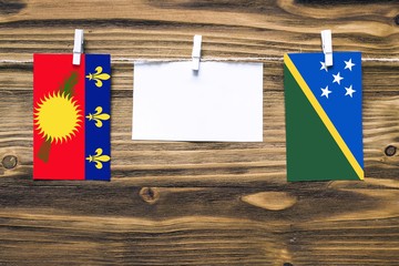 Hanging flags of Guadeloupe and Solomon Islands attached to rope with clothes pins with copy space...