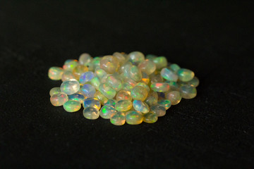 Opals gemstone from Ethiopia lies on black background. White fire opals with rainbowlike fire. Natural fire Ethiopian opal, small stones to create jewelry. Handmade stone jewelry. A pile of stones
