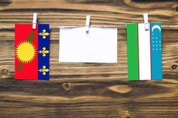 Hanging flags of Guadeloupe and Uzbekistan attached to rope with clothes pins with copy space on...