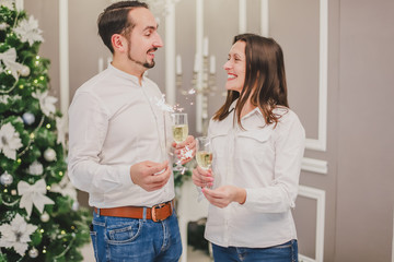 Loving and stylish couple in holiday atmosphere, standing with bengal lights, drinking champange.