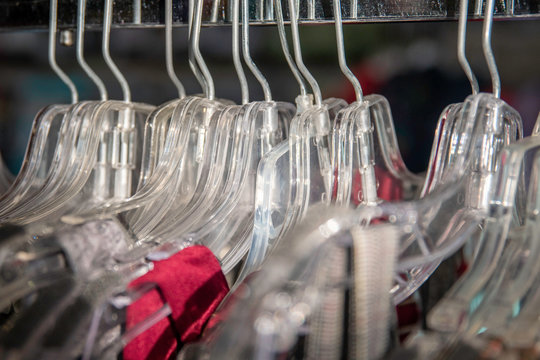 Clear plastic hangers on a rack in a store with the straps of a red dress.