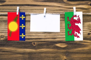 Hanging flags of Guadeloupe and Wales attached to rope with clothes pins with copy space on white...