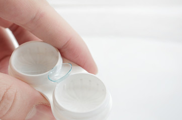 the girl is holding a container for soft contact lenses and a lens on her finger