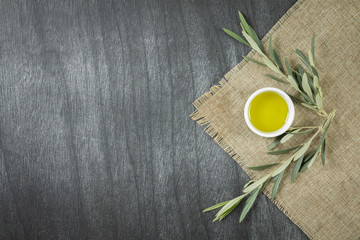 Top view of olive oil in a bowl, on wooden background. Olive oil with branches. Natural olive oil in white plate with branches around. Copy space for text or product.