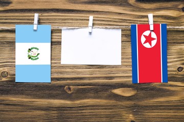 Hanging flags of Guatemala and North Korea attached to rope with clothes pins with copy space on white note paper on wooden background.Diplomatic relations between countries.