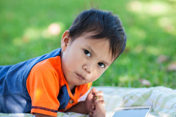 A latino boy taking a break from playing educational games on his tablet, while laying down on the lawn.
