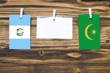 Hanging flags of Guatemala and Mauritania attached to rope with clothes pins with copy space on white note paper on wooden background.Diplomatic relations between countries.