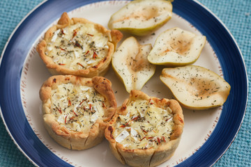 Puff pastry julienne with mushrooms and camembert cheese. Sliced sweet pear. White decorative plate with blue border. Traditional cuisine. Tapas. 