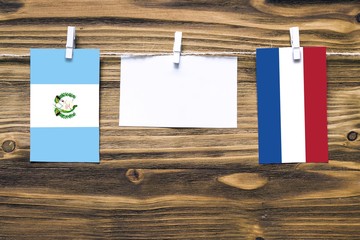 Hanging flags of Guatemala and Netherlands attached to rope with clothes pins with copy space on white note paper on wooden background.Diplomatic relations between countries.