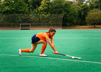Female hockey player attacking and hitting on a grass field.