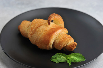 croissant on a black plate and a mint leaf -