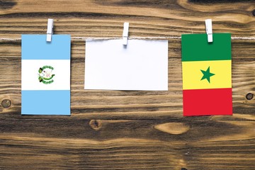 Hanging flags of Guatemala and Senegal attached to rope with clothes pins with copy space on white note paper on wooden background.Diplomatic relations between countries.