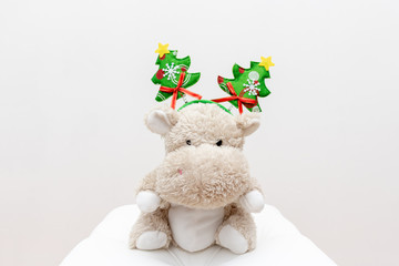 Cute teddy hippo, soft stuffed toy with christmas decoration of funny christmas tree on a head on white background
