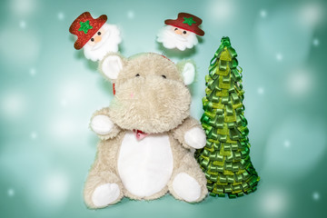 Cute teddy hippo, soft toy with christmas decoration on a head and a christmas tree