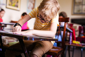Blonde boy with glasses drawing. Group of elementary school pupils in classroom on art class....