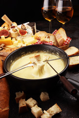 Gourmet Swiss fondue dinner on a winter evening with assorted cheeses on a board alongside a heated...