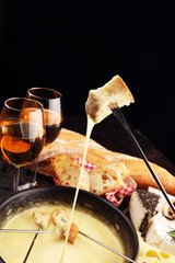 Gourmet Swiss fondue dinner on a winter evening with assorted cheeses on a board alongside a heated pot of cheese fondue with two forks dipping
