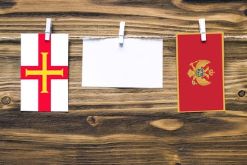 Hanging flags of Guernsey and Montenegro attached to rope with clothes pins with copy space on white note paper on wooden background.Diplomatic relations between countries.