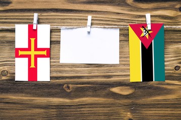 Hanging flags of Guernsey and Mozambique attached to rope with clothes pins with copy space on...