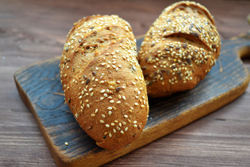 Two bread rolls sprinkled with seeds and caraway on rustic wooden table