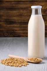 Bottle of soy milk with soybeans on white table over dark wooden background