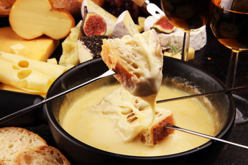 Gourmet Swiss fondue dinner on a winter evening with assorted cheeses on a board alongside a heated pot of cheese fondue with two forks dipping