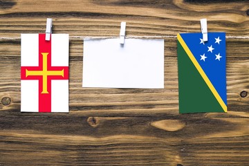 Hanging flags of Guernsey and Solomon Islands attached to rope with clothes pins with copy space on...