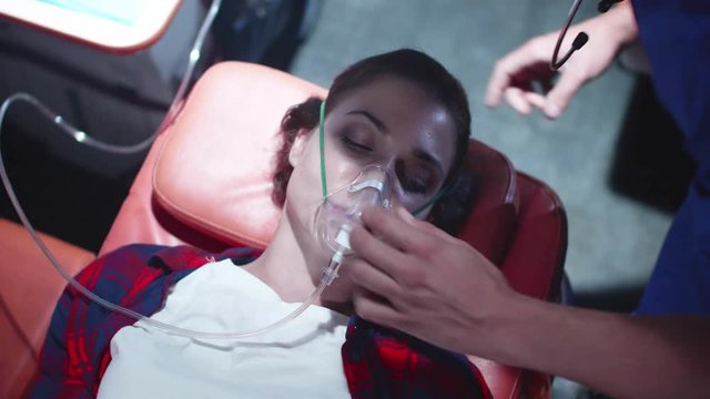 Young woman in ambulance, corpsman put on her face mask.