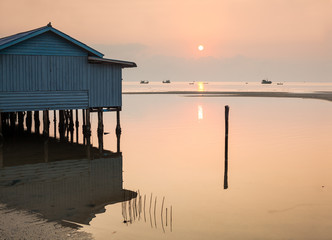 Seascape at sunrise with traditional wooden house on stilts and calm pink sea and sky, Prek Svay, Koh Rong island, Cambodia