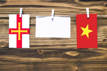 Hanging flags of Guernsey and Vietnam attached to rope with clothes pins with copy space on white note paper on wooden background.Diplomatic relations between countries.