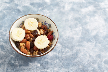 Bowl of granola with nuts, raisins and banana. Concept for a tasty and healthy meal. Rustic wooden background. Copy space. 