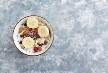 Bowl of granola with nuts, raisins and banana. Concept for a tasty and healthy meal. Rustic wooden background. Copy space. Top view. 