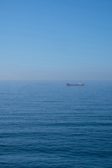 Cloudy horizon and Fog over the sea waves, natural background, red cargo ship on the horizon