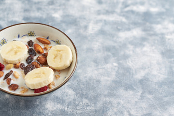 Bowl of granola with milk, nuts, raisins and banana. Concept for a tasty and healthy meal. Rustic wooden background. Copy space. 