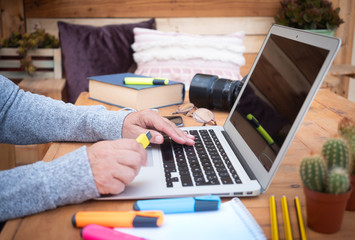 Side view of senior woman's hands working on laptop. Wooden table. Alternative outdoor office. Book, devices and camera close to her