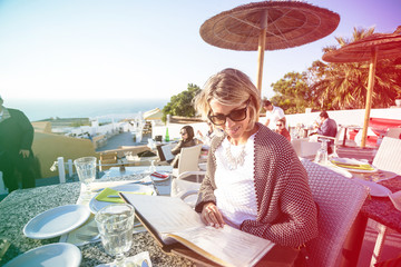 Fototapeta na wymiar Attractive blond brazilian woman with sunglasses looking at menu on a beautiful spring day in Mykonos. Colored light leak