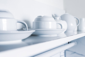 White ceramic coffee cups and saucers standing in a row on a shelf in kitchen