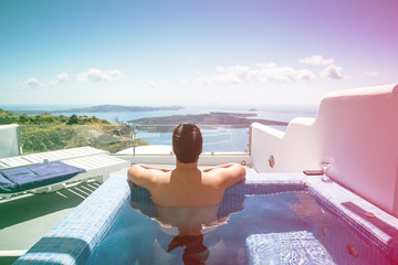 Dark haired man relaxing and contemplating beautiful scene from private pool in one of Oia,...