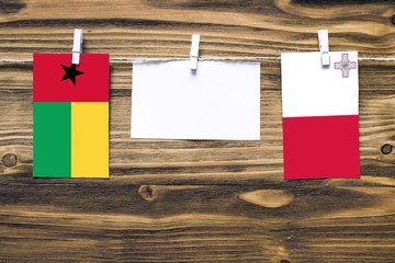 Hanging flags of Guinea Bissau and Malta attached to rope with clothes pins with copy space on white note paper on wooden background.Diplomatic relations between countries.