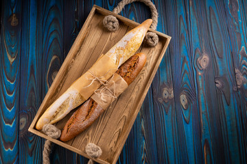 Two baguettes from wheat and buckwheat flour on a vintage tray on a blue wooden background.